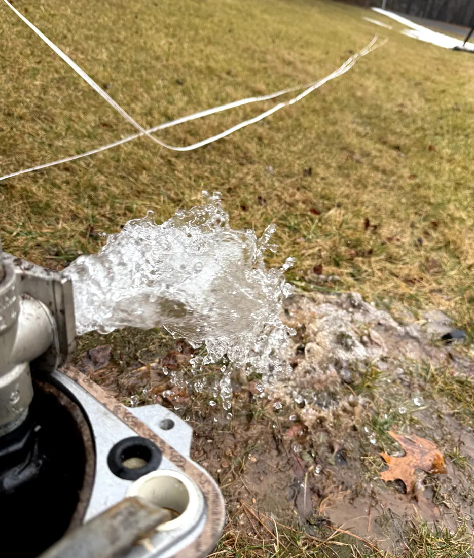 Clear water gushing from a well line onto a lawn during a flush