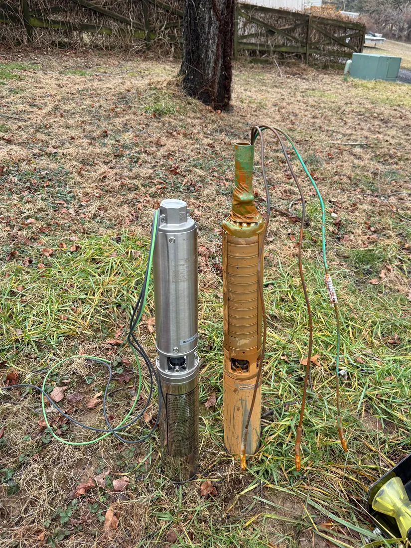 An old rusted submersible pump standing next to a new stainless pump on a lawn