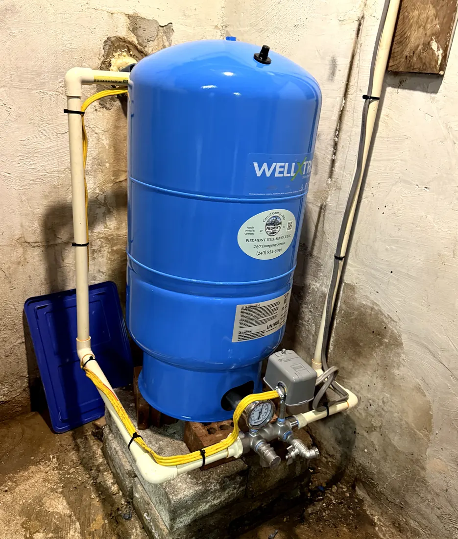 A new blue well pressure tank and fittings installed on a basement floor