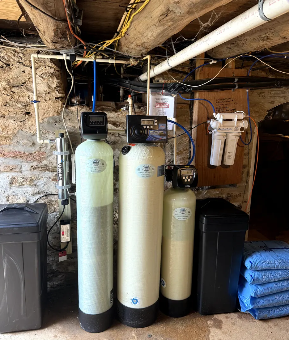 Three water treatment tanks with control heads and a salt tank installed in a stone-walled basement