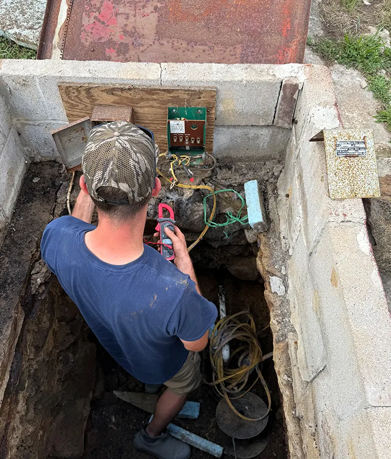 A Piedmont technician testing wiring with a meter inside a block well pit